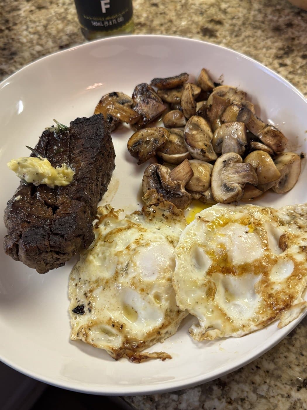 Steak with garlic herb butter, sautéed mushrooms and two fried eggs on a white plate