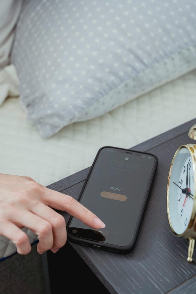 Cell phone sitting on nightstand. A woman is turning off the alarm.