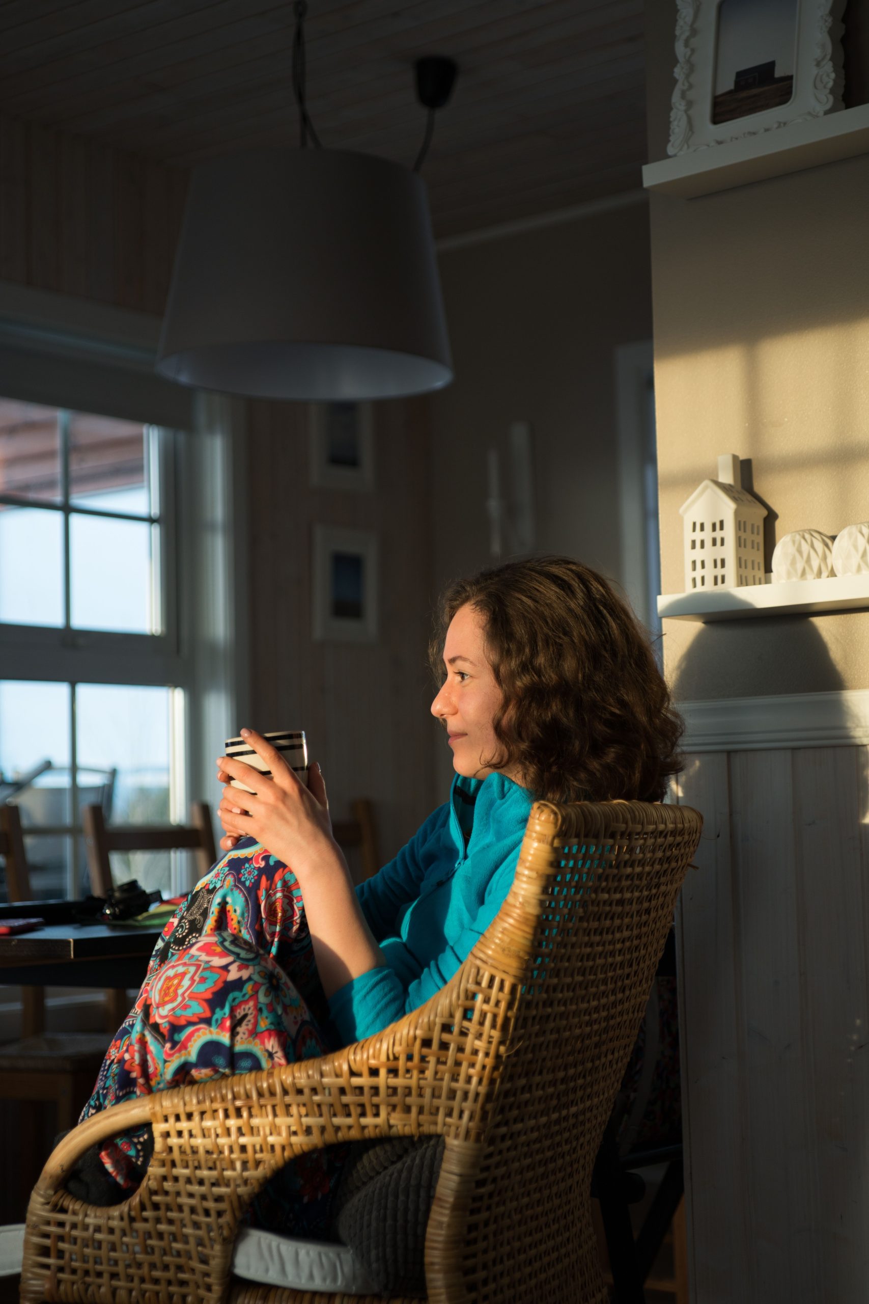 Midlife woman sitting in a chair in the morning sunlight while sipping coffee.